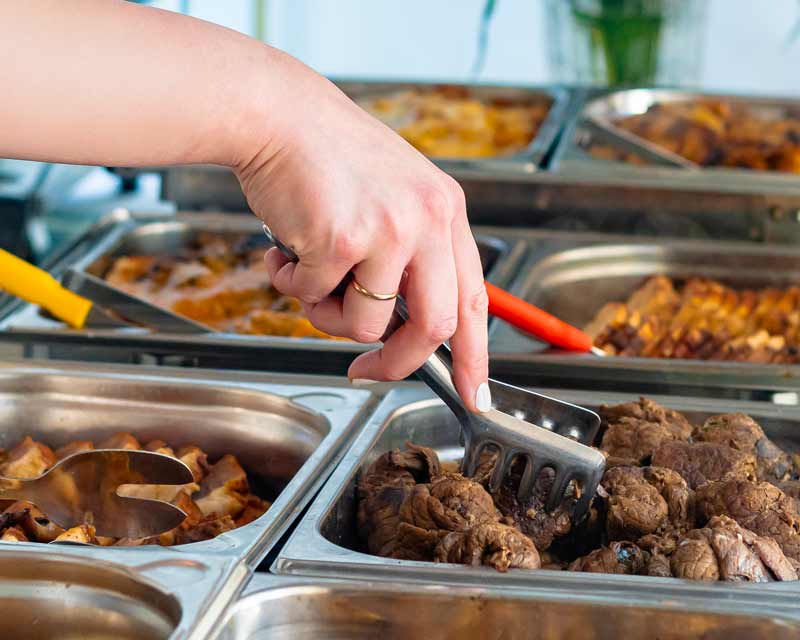 Person nimmt Fleisch aus einem Buffet-Warmhaltebehälter