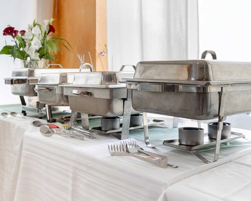 Karriere 1 Buffet mit geschlossenen Warmhaltebehältern und Besteck auf weiß gedecktem Tisch