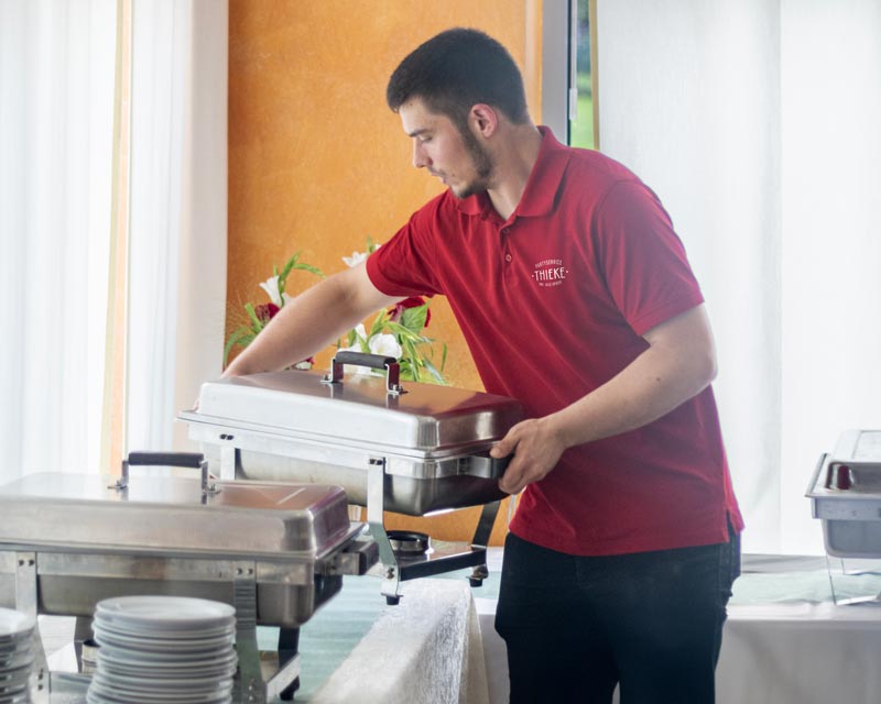 Nils Spieß stellt Warmhaltebehälter auf ein Buffet