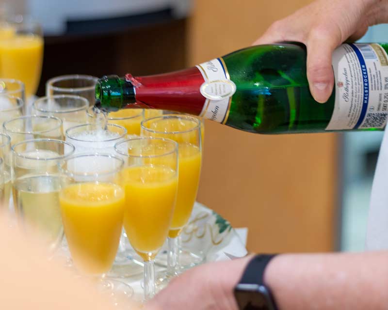 Landingpage Rhede 6 Hand schenkt Sekt in Gläser mit Orangensaft auf Tablett